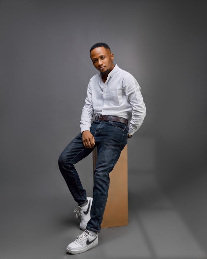 services-03 Fashionable male model posing in a studio wearing a white shirt, jeans, and sneakers against a gray background.