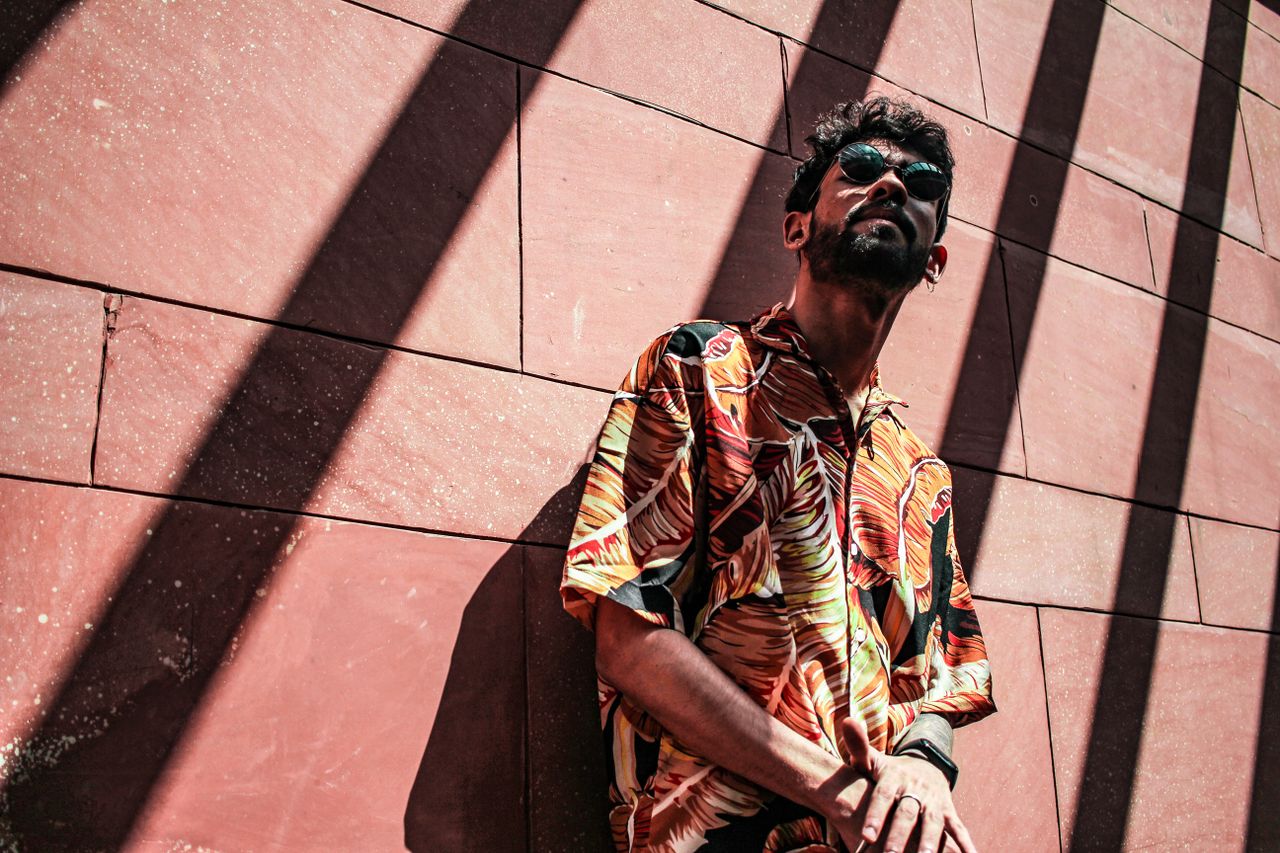 services-01 A man wearing a vibrant tropical shirt poses confidently against a wall, casting strong shadows.