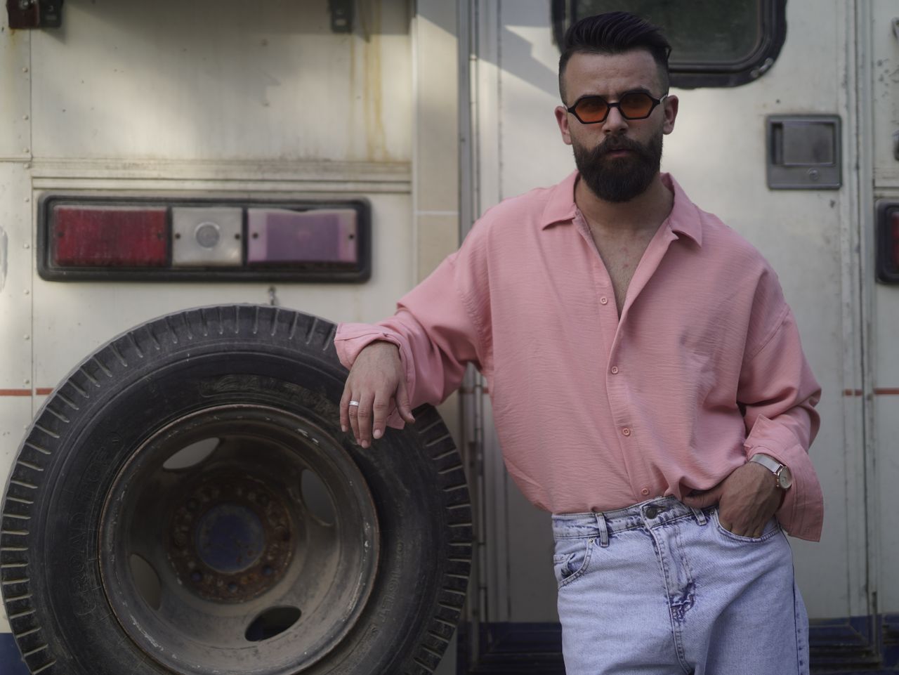 services-02 A stylish man in sunglasses and pink shirt leans against a tire, showcasing a relaxed yet fashionable look.